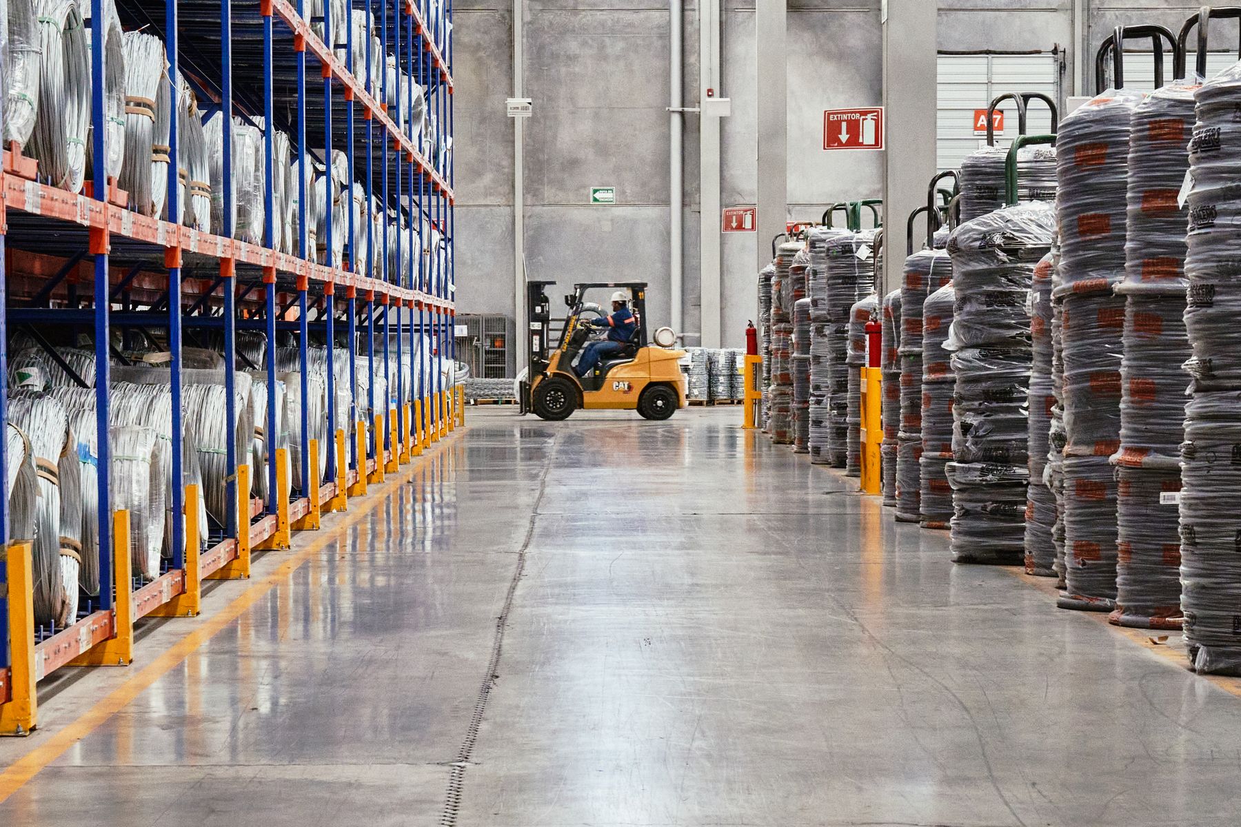 Forklift operating in an industrial warehouse aisle with stocked shelving and material pallets